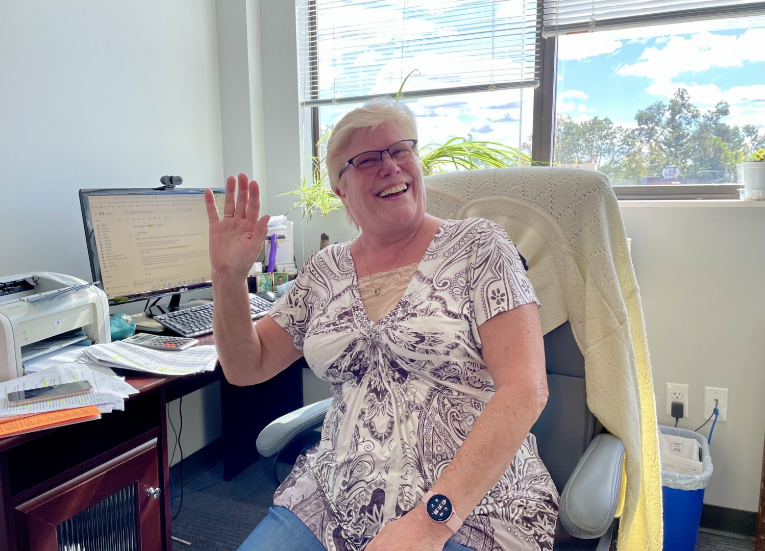 Loraine, the Arts for Learning Program Manager, sits at her desk waving and smiling.
